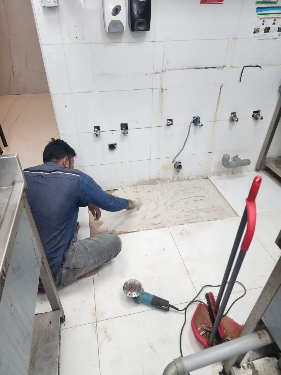 Technician carrying out drain blockage repair work in a tiled service area