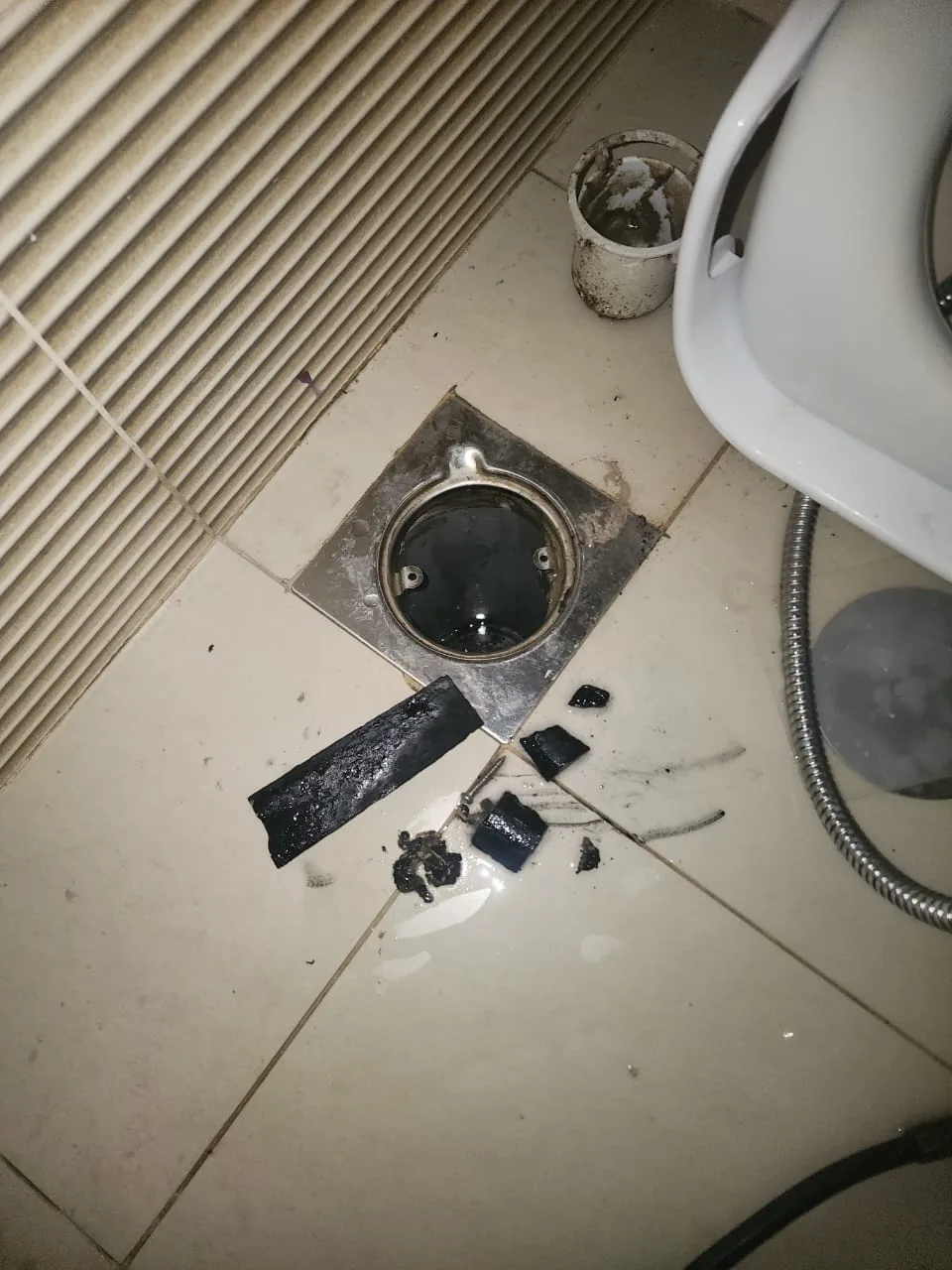Opened floor drain with removed blockage debris beside bathroom fixture